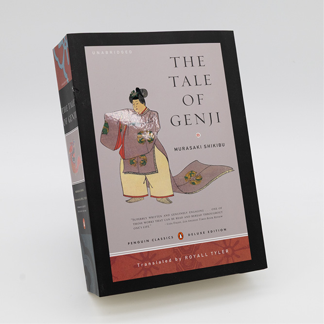 Front cover of ‘The Tale of Genji’ by Murasaki Shikibu, deluxe edition, featuring a traditional illustrated figure against a soft grey background, photographed standing upright on a white surface.
