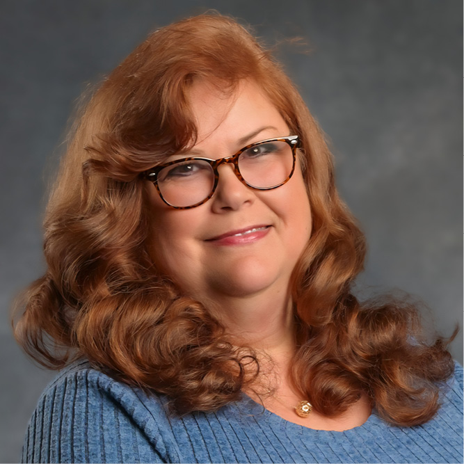 Studio portrait of a person with shoulder-length red curls, wearing a blue knit top against a neutral backdrop.