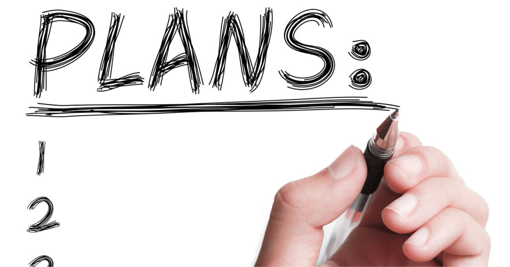 Hand holding a pen, writing “Plans” and underlining it on a clean white background as the start of a list.