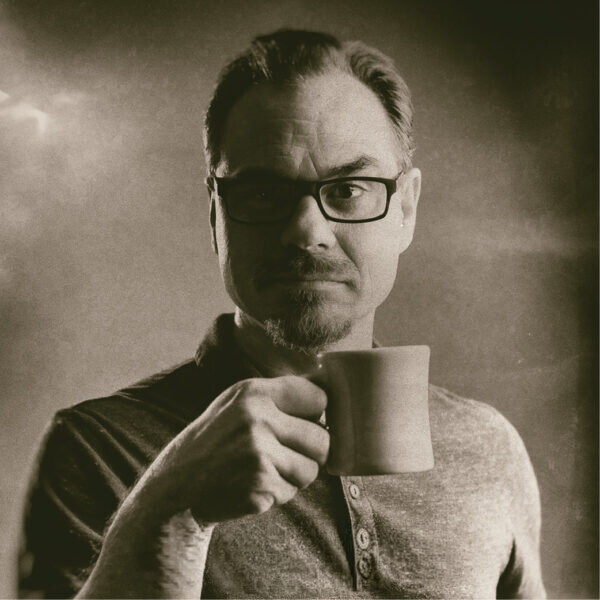 Person holding a coffee mug in a sepia-toned, vintage-style portrait.