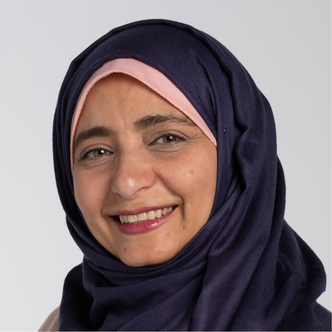 Individual wearing a dark hijab against a light gray background.