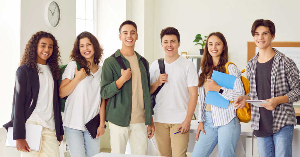 Group of students standing indoors with backpacks and notebooks, appearing ready for class or a school activity.