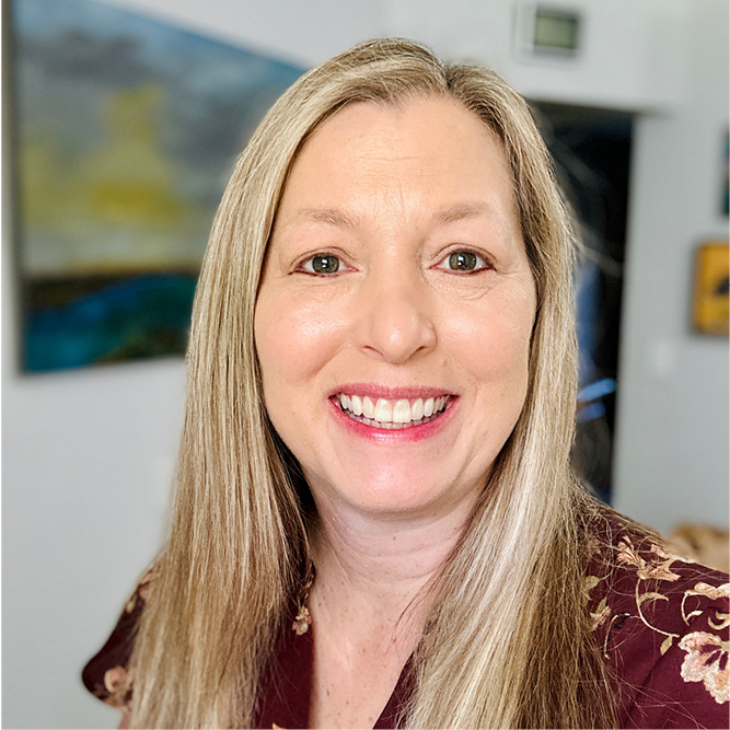 Individual with long blonde hair standing in a room with artwork on the wall.