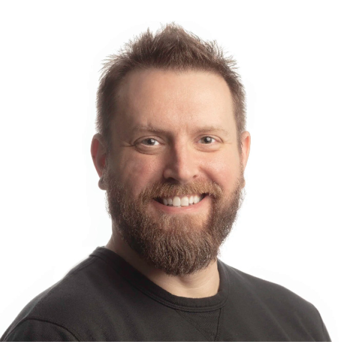 Person with short hair and a beard wearing a dark shirt against a white studio background.