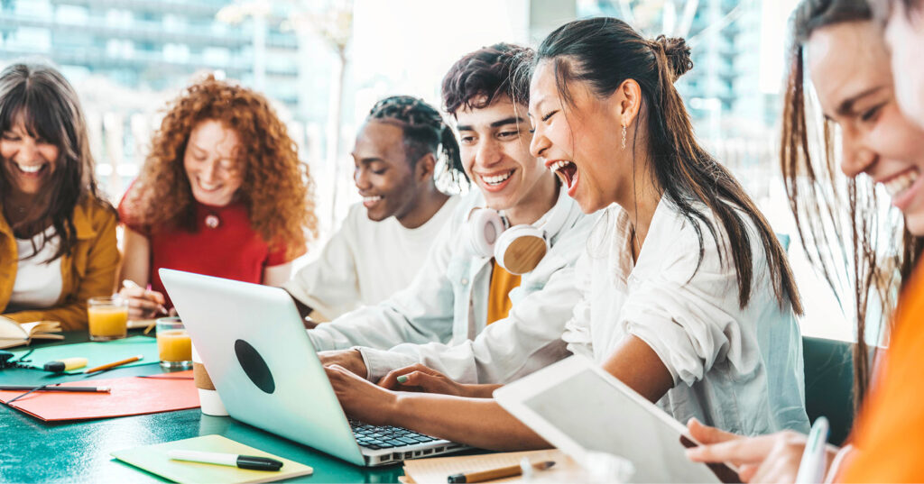Diverse group collaborating around a table with laptops and tablets in a bright, modern workspace.