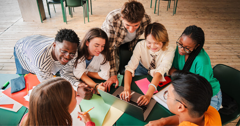 Group collaborating around a table, reviewing notes and working together on a laptop in a shared workspace.