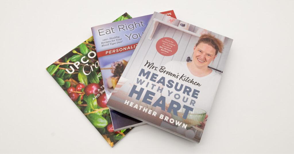 Stack of cookbooks arranged on a white surface, with colorful covers and titles related to cooking and healthy eating.