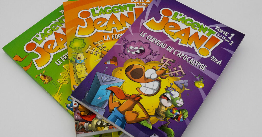 A fan‑shaped stack of brightly colored L’Agent Jean! comic books, featuring energetic cartoon characters on green, yellow, and purple covers.