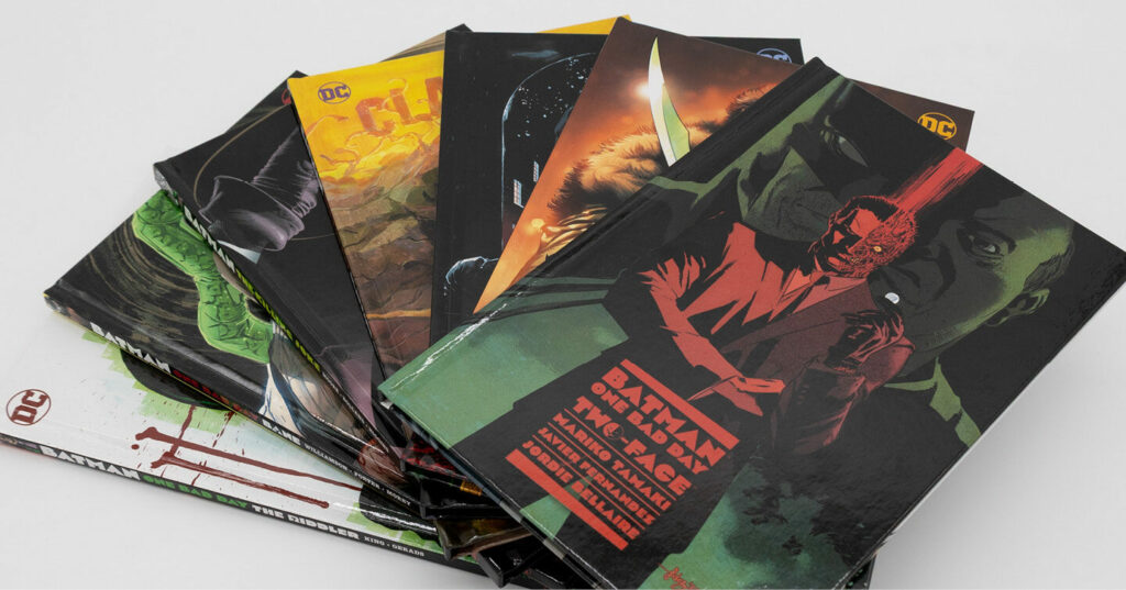 A fan‑shaped stack of DC comic books laid out on a surface, featuring bold illustrated covers including Batman and other characters.