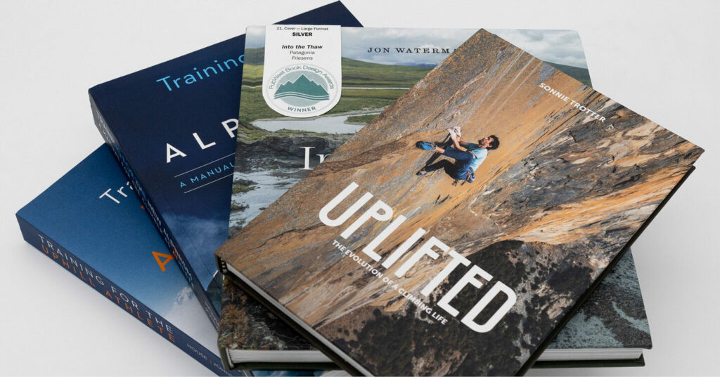 A small stack of hardcover books arranged in a fan, including a climbing‑themed book titled UPLIFTED on top.