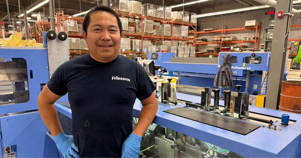 Employee-owner standing beside book finishing equipment on the production floor at Friesens.