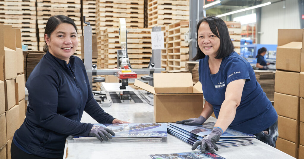 Employee-owners stacking and packaging printed books at a work table on the production floor at Friesens.