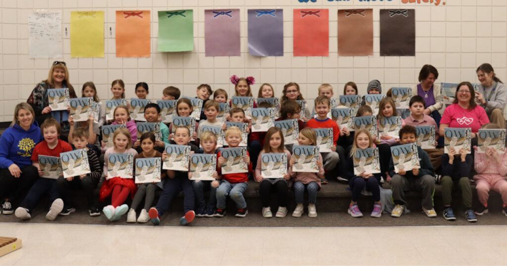 Grade 2 students seated together in a school gym, holding copies of Owl during an I Love to Read Month visit.