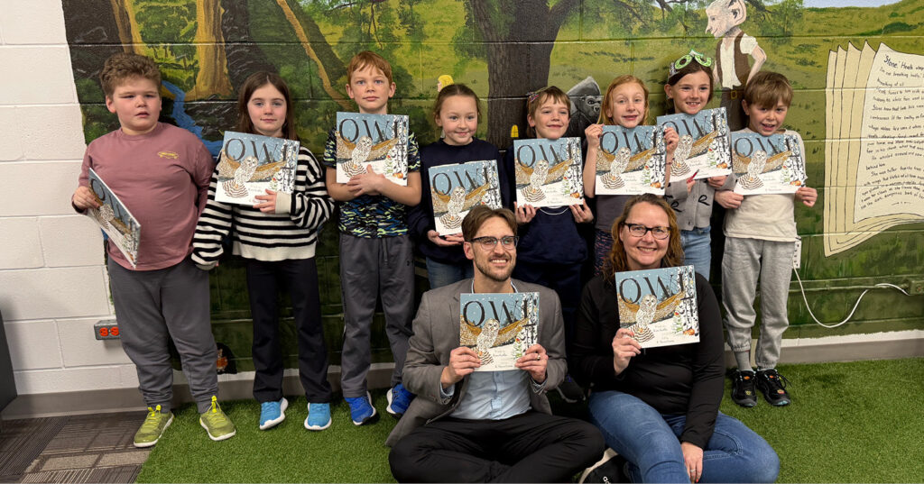 Group of Grade 2 students standing together, holding copies of Owl in front of a colourful classroom mural.