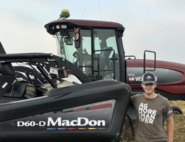A young man stands beside a large piece of farming equipment.