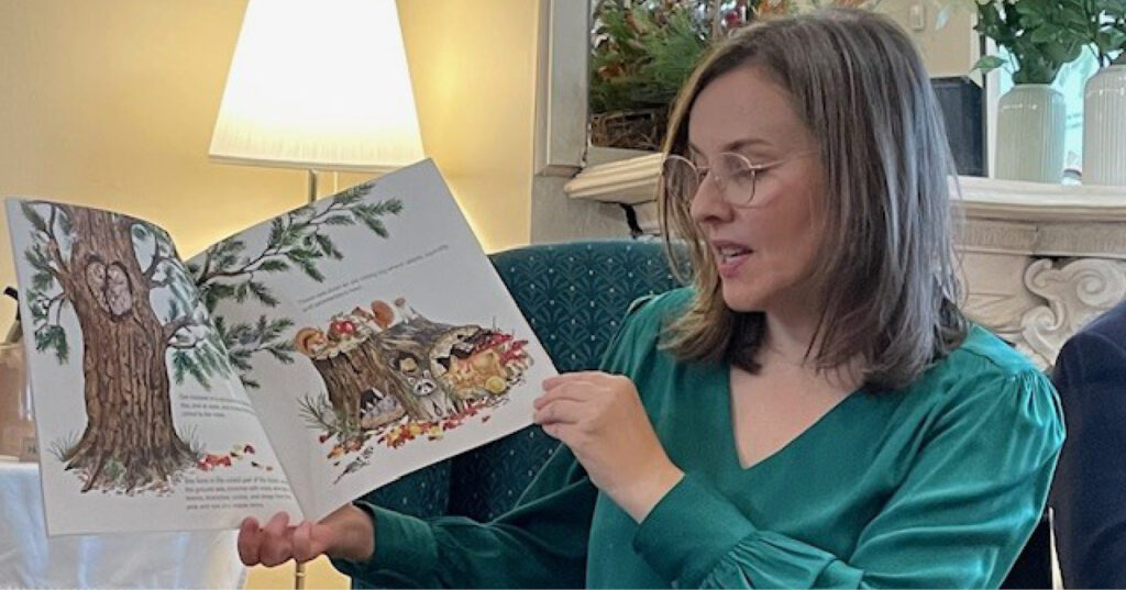 Adult reading Owl aloud from an open picture book, showing illustrated woodland animals during a reading session.