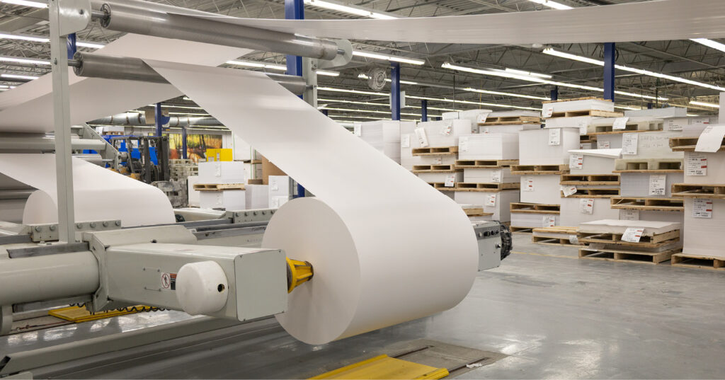A roll of bright white paper feeding through sheeting equipment, showing how paper shade appears under production lighting.