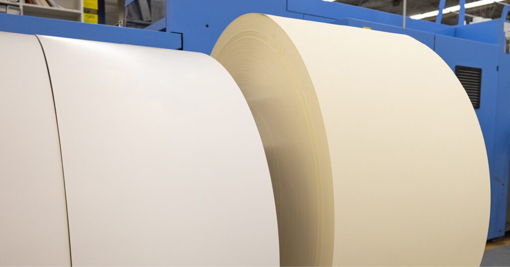 Large rolls of paper showing a bright white sheet beside a warmer, cream‑toned sheet to illustrate paper shade differences.
