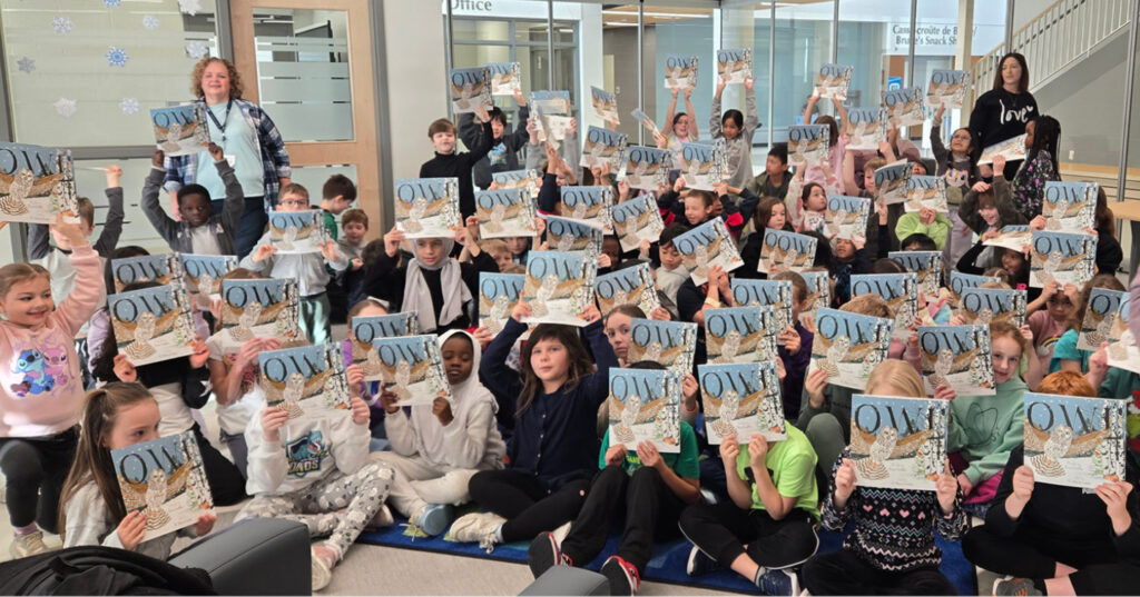 Large group of Grade 2 students holding copies of Owl and raising books in the air during an I Love to Read Month celebration.