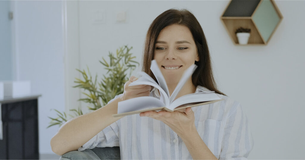 Person sitting indoors, holding an open book and turning pages in a calm, modern living space.