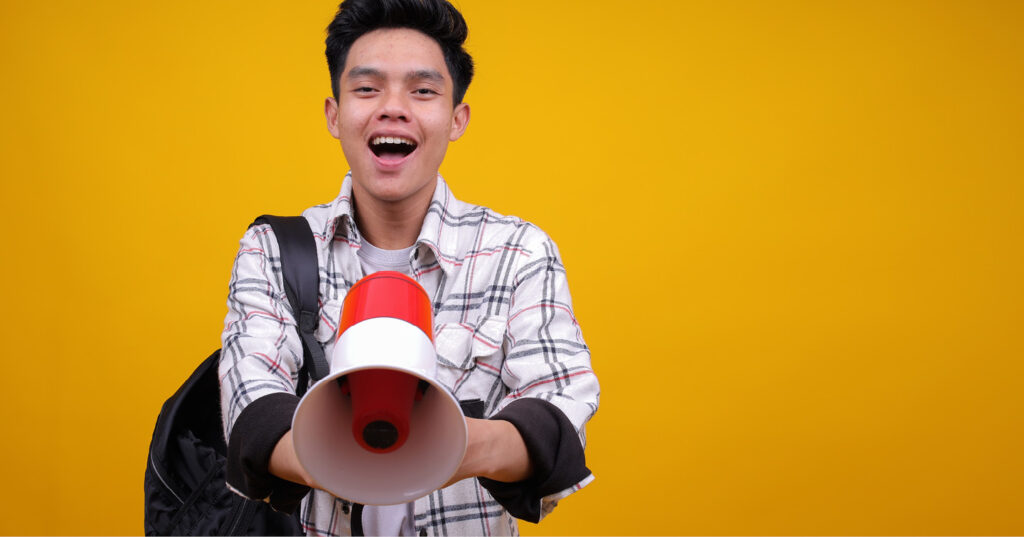 Person holding a red and white megaphone, wearing a plaid shirt and backpack, against a yellow background.