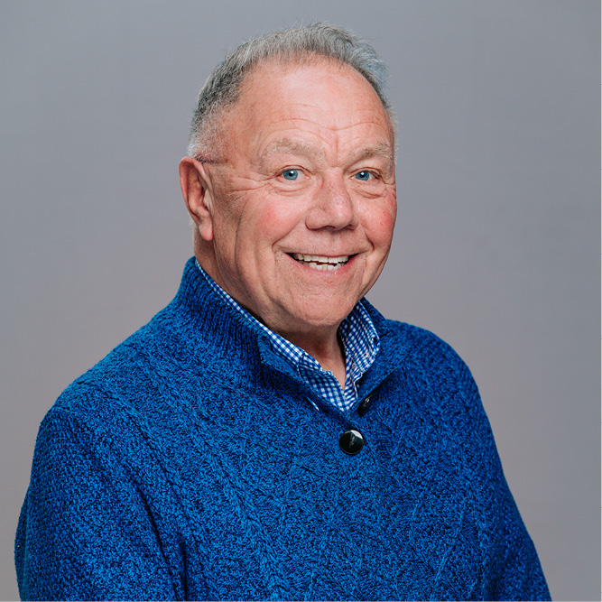 Portrait of an older person in a blue sweater, facing forward against a neutral background.