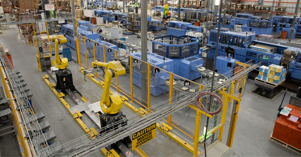 Automated book production line with robotic arms moving materials between blue machines in large printing facility