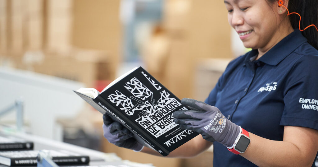 Employee-owner wearing gloves inspects finished black-and-white printed book on production line in print facility
