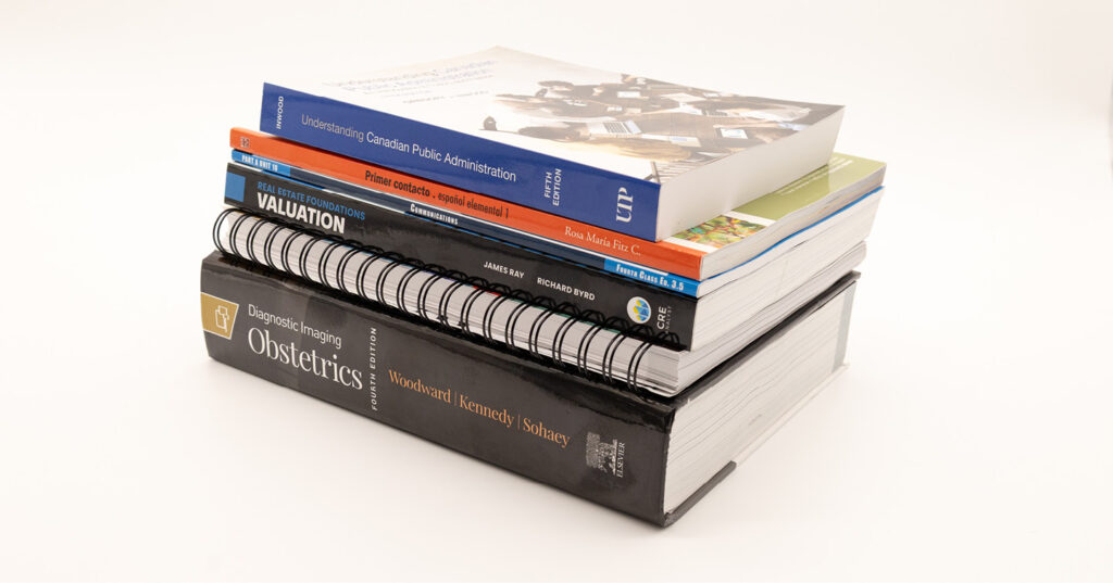 Stack of educational textbooks showcasing multiple binding styles, including hardcover, softcover, and spiral-bound formats.