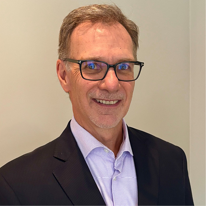 Professional head-and-shoulders portrait of a person wearing glasses and a suit jacket against a plain light-coloured background.