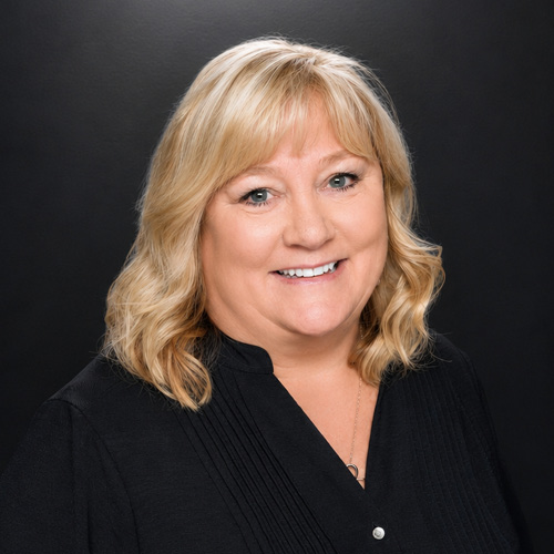 Professional headshot of a person wearing a black blouse against a dark studio background.