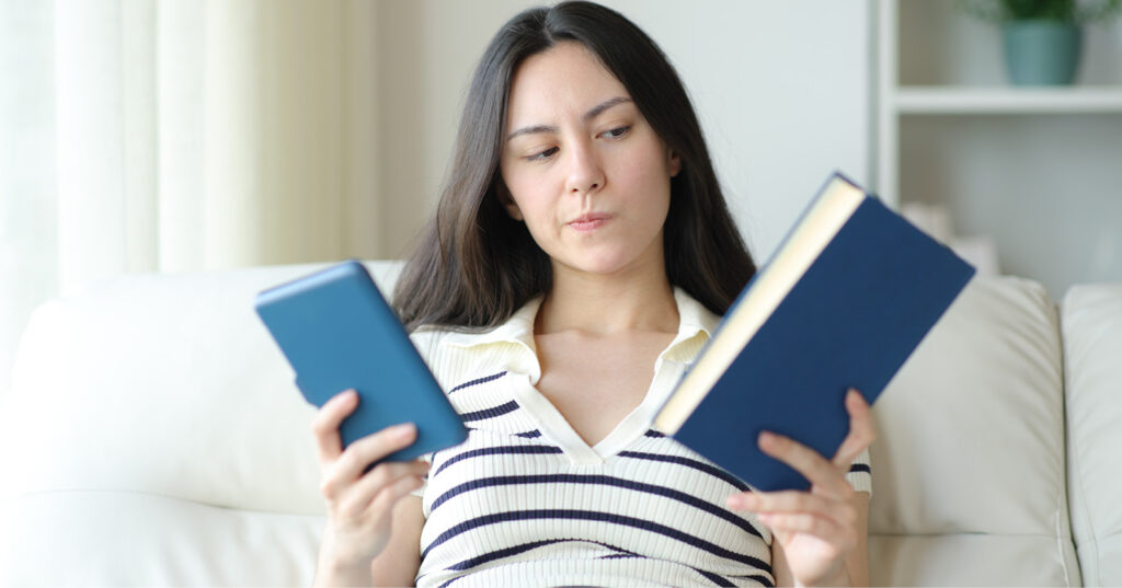 Person comparing a printed book and an e-reader while seated indoors, highlighting reading format choices.