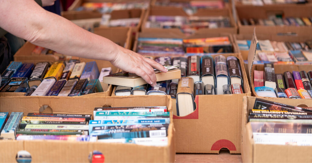 Person browsing donated books arranged in cardboard boxes at a community book sale or reuse event.