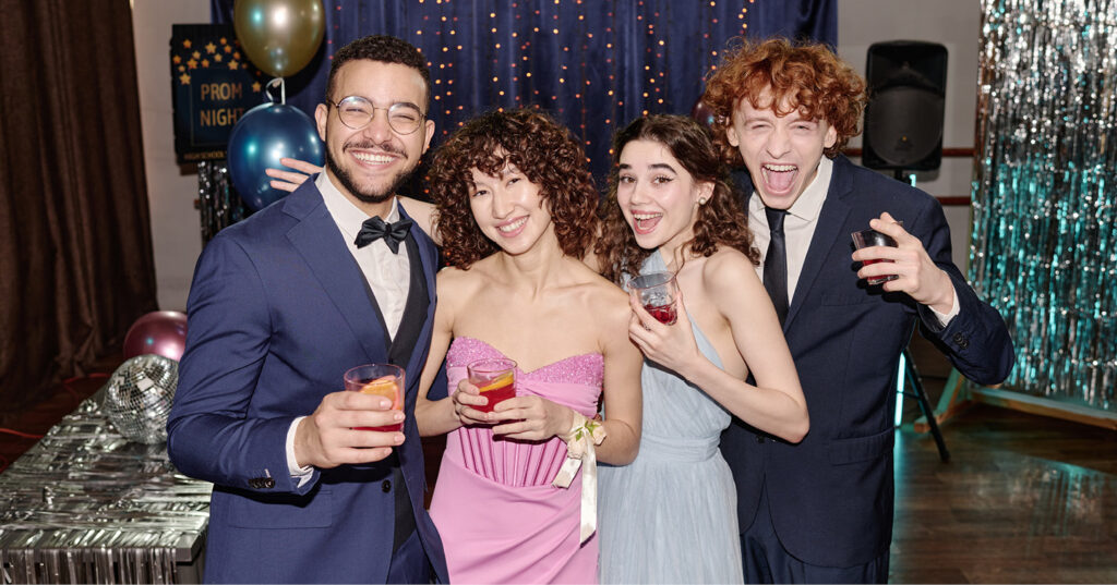 Students dressed for prom pose together with drinks and decorations at a school dance celebration.