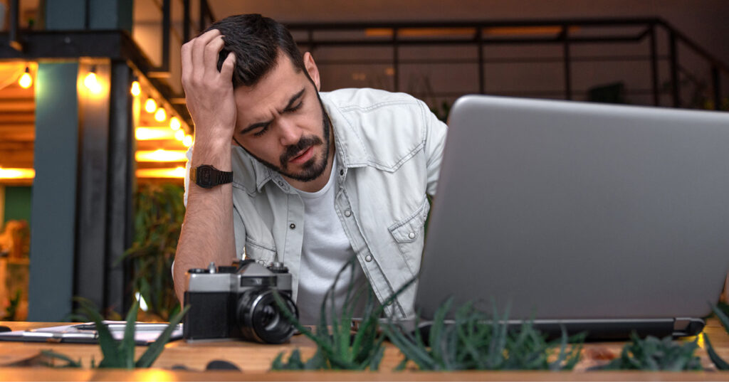Person reviewing photos on a laptop beside a camera, illustrating the challenge of managing many images.