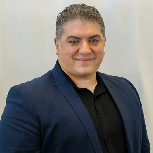 Professional headshot of a person wearing a blue blazer and black shirt against a light background.