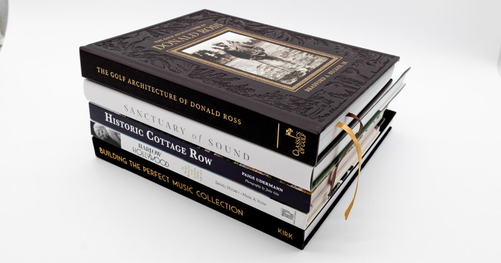 Stack of premium hardcover coffee table books featuring embossed covers, foil stamping, and ribbon bookmarks.