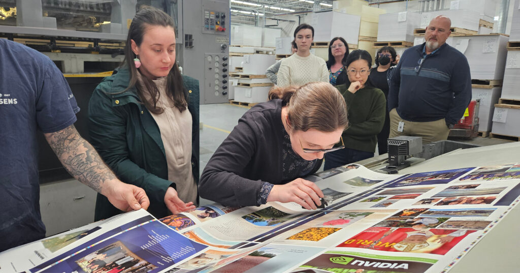 Person using a loupe to inspect colour and print quality on press sheets while a group observes the press check.